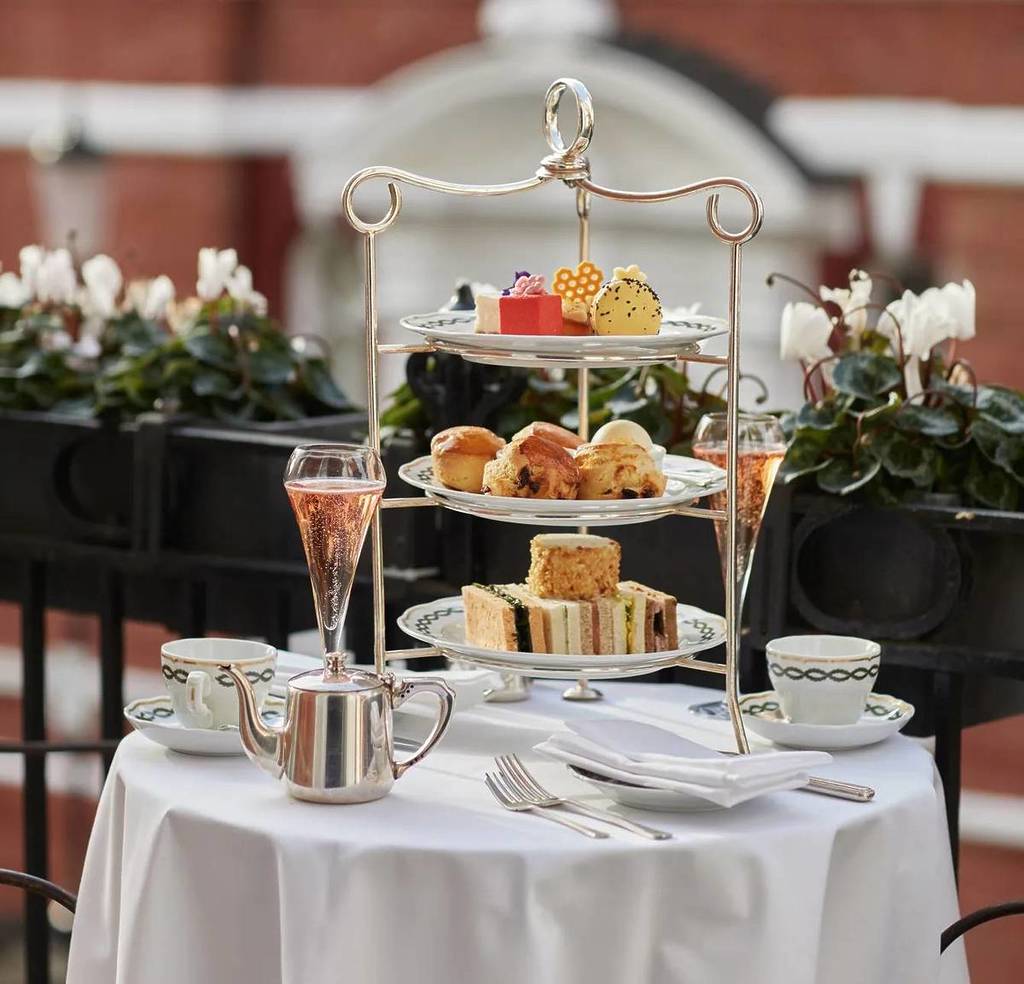 uma bandeja com andares com sanduíches, scones e bolos, acompanhados por copos de champanhe