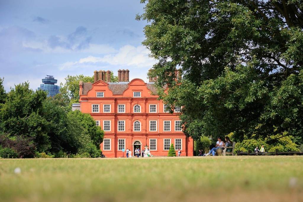 Ein rotes Backsteingebäude, versteckt hinter zwei großen Bäumen und einem grünen Rasen