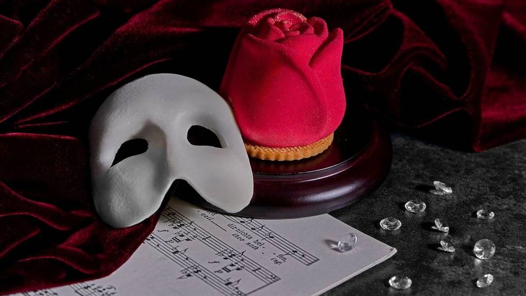 doces em forma da máscara branca do Fantasma da Ópera e de uma rosa vermelha, apresentados ao lado de uma partitura