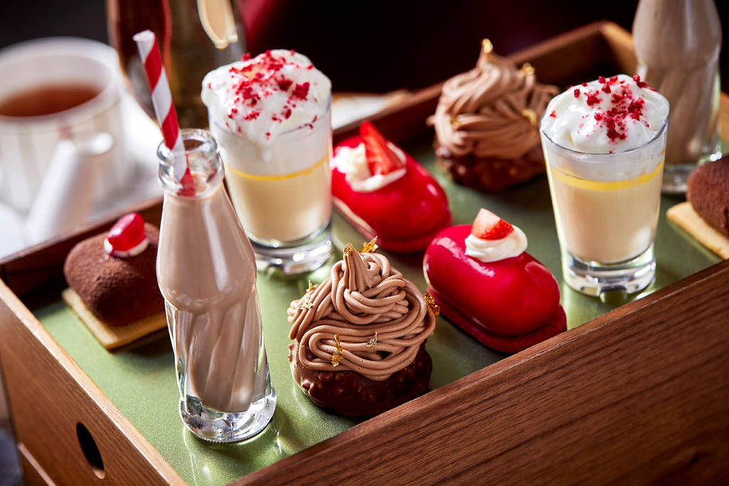 uma variedade de doces e bolos numa bandeja, ao lado de «garrafas de refrigerante» cheias de uma bebida semelhante a leite com chocolate