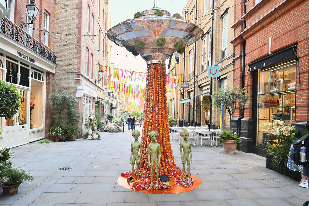 a floral installation in the streets of chelsea showing a trio of martians at the base of a 'ufo beam' below a hovering spacecraft