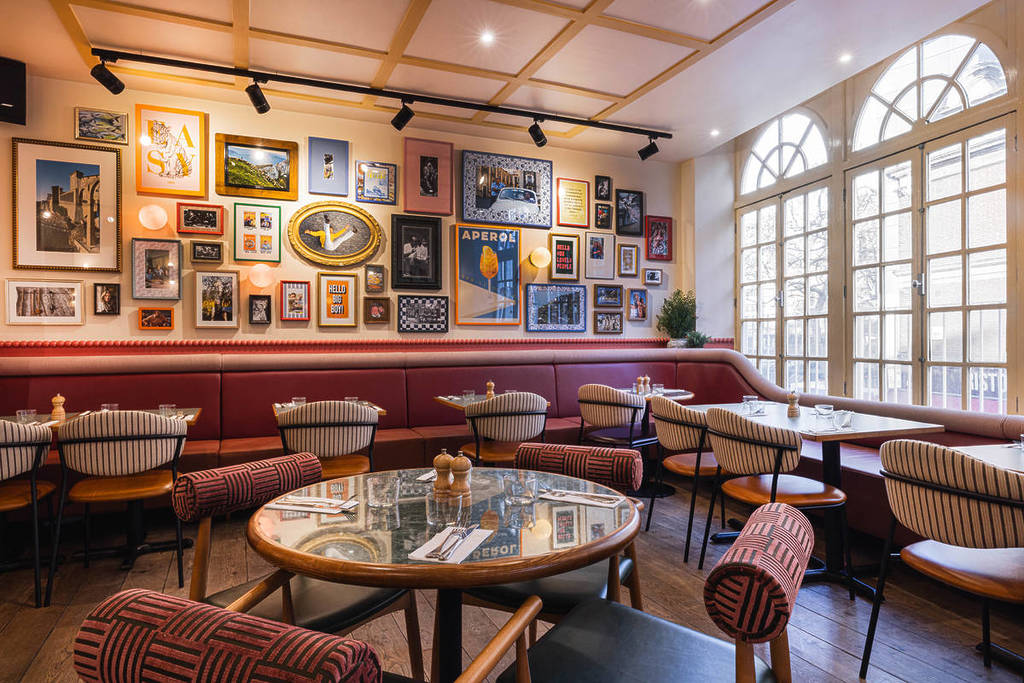 Tafels binnen bij Jamie's Italian, met grote ovale ramen en foto's aan de muren