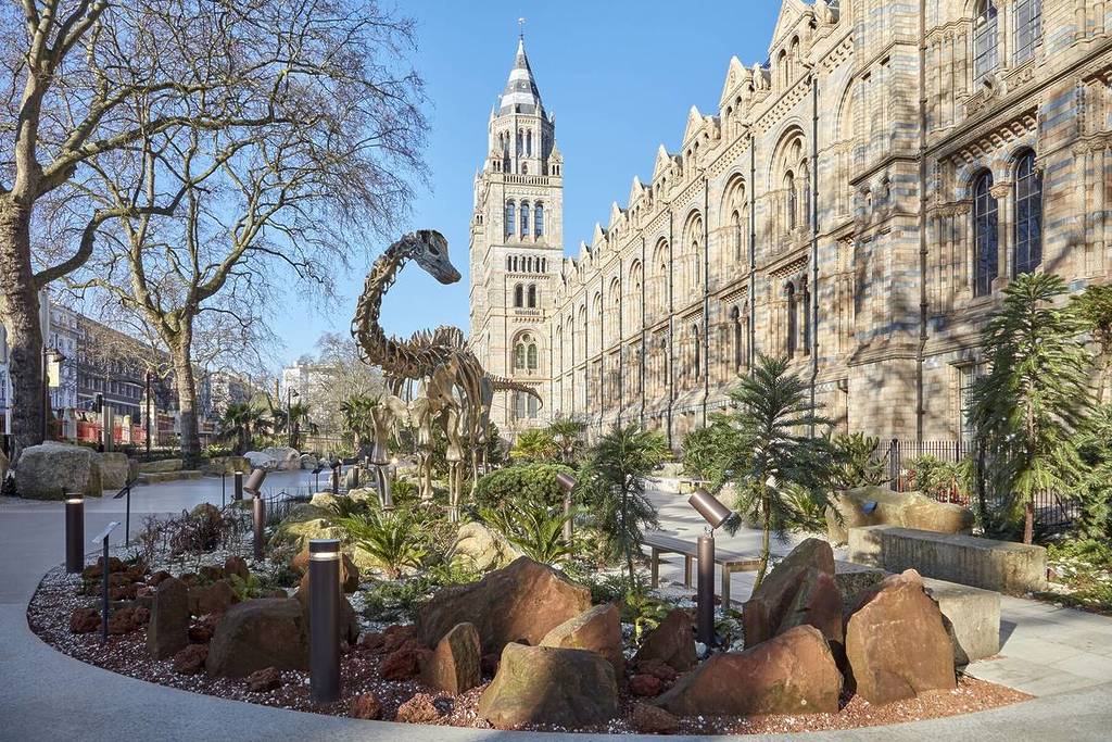 die Gärten des Naturhistorischen Museums, mit einem Dinosaurierskelett im Laubwerk, im Hintergrund ist das Museum zu sehen