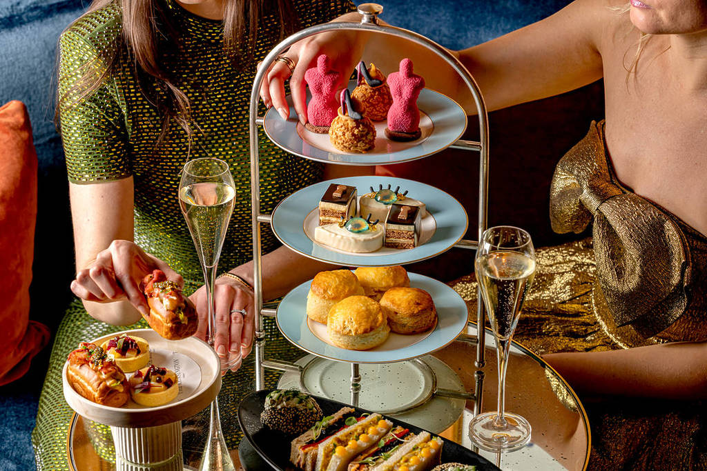 Zwei Personen saßen um einen Tisch, der für den Nachmittagstee gedeckt war, mit kunstvoll verziertem Gebäck und süßen Leckereien auf einem gestuften Tablett, Scones, herzhaften Sandwiches und Gläsern Champagner