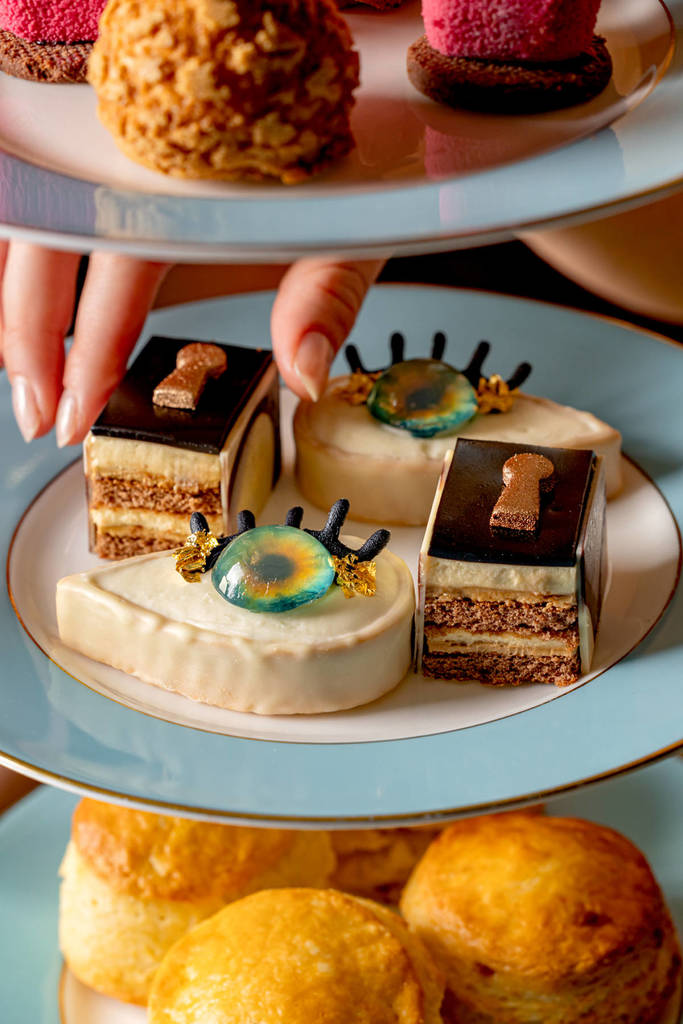 una mano que se extiende para coger un pequeño pastelito de un plato de dulces, entre los que se encuentra uno con forma de ojo
