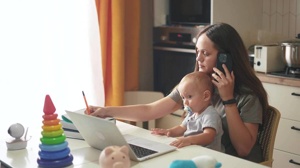 mother with a child sits at a table and works on a laptop