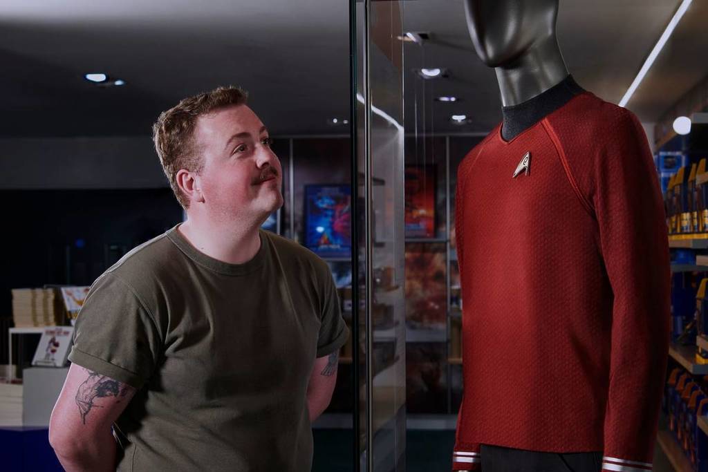 Ein Mann schaut auf und lächelt über ein ausgestelltes rotes Star Trek-Kostüm