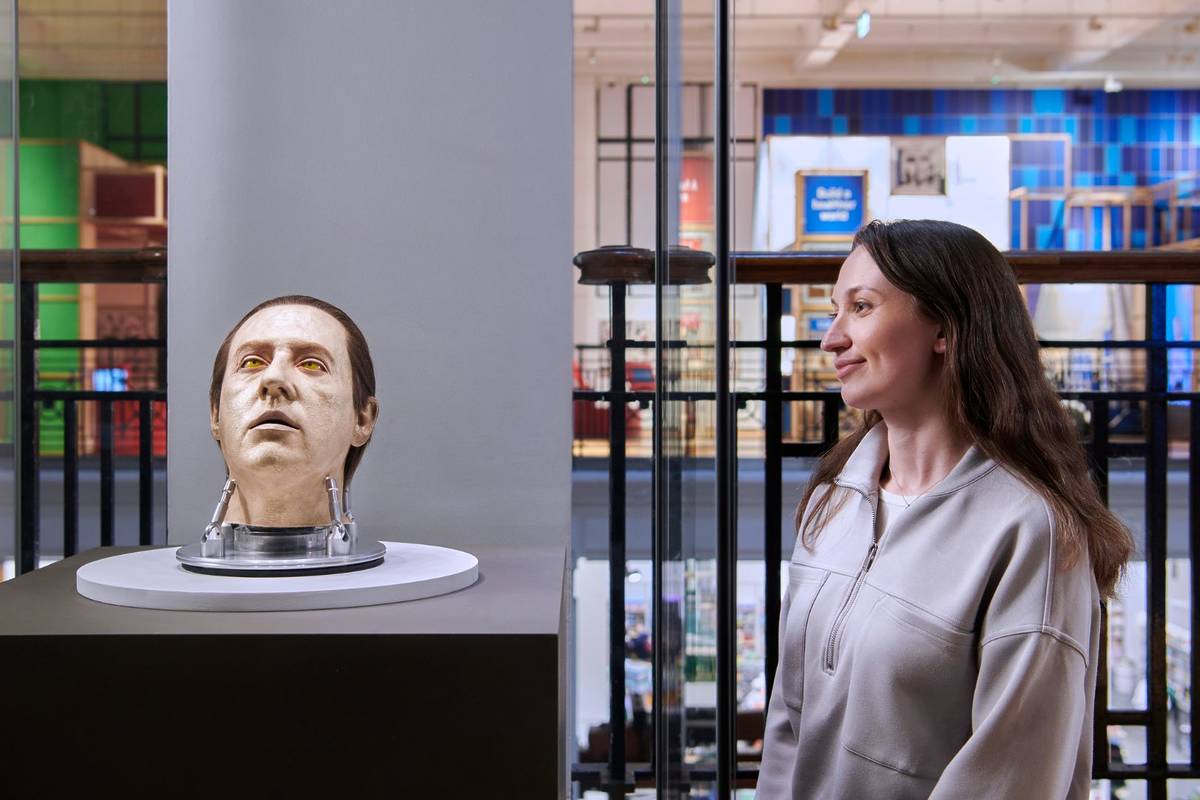 Uma mulher observa uma cabeça de adereço atrás de um vidro.