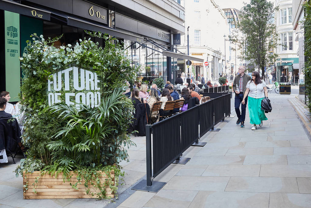 people sat in an outdoor dining area next to sign in a bush reading 'future of food'