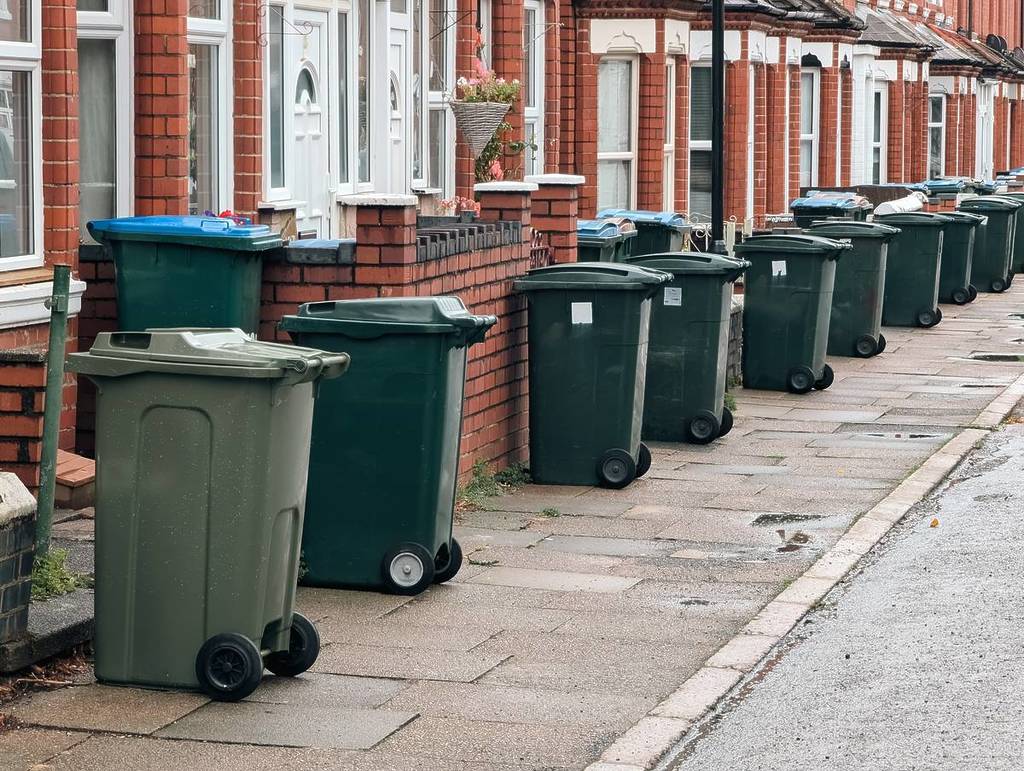 Reihe grüner Mülltonnen, aufgereiht in einer Wohnstraße, bereit zur Abholung.