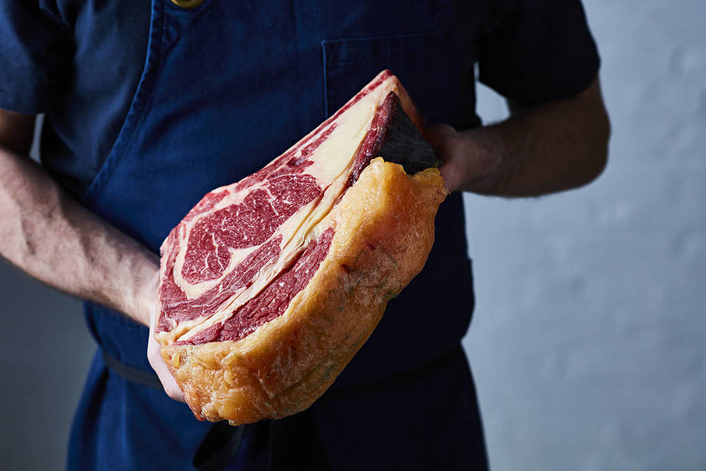 someone holding an enormous raw steak with an impressive fat cap