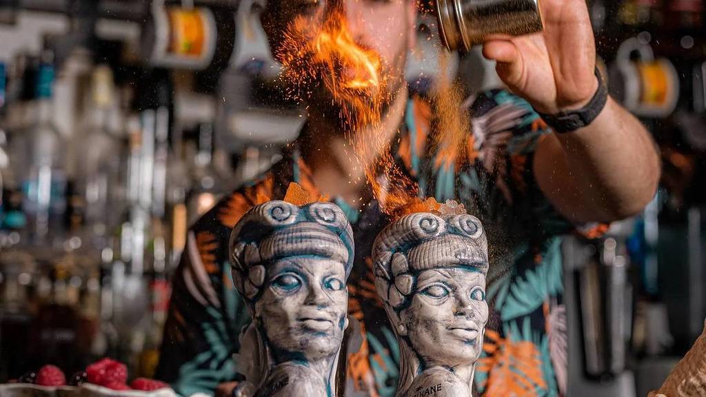 un barista che dà gli ultimi ritocchi a due cocktail in speciali bicchieri tiki