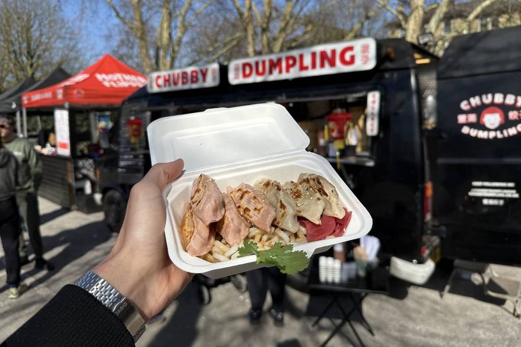 Eine Schachtel Knödel wird vor einen Imbisswagen gehalten, auf dem die Worte stehen 