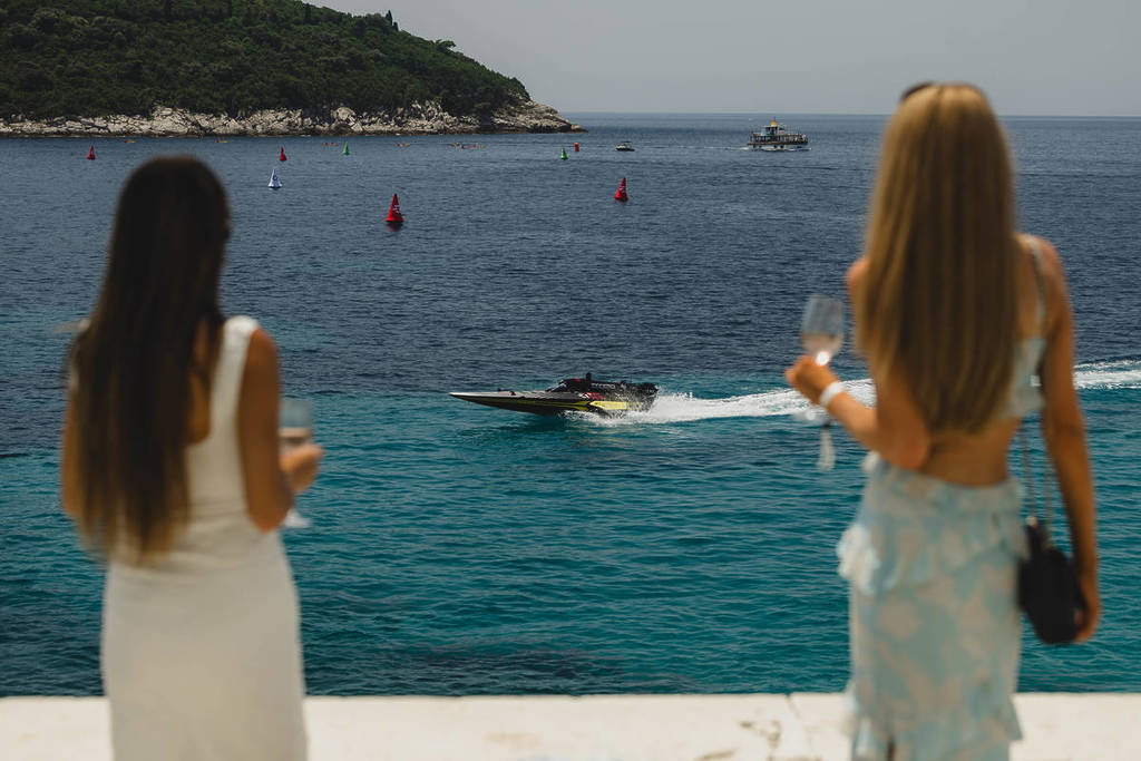 dos mujeres con copas de champán en la mano observan cómo un barco surca las aguas a toda velocidad