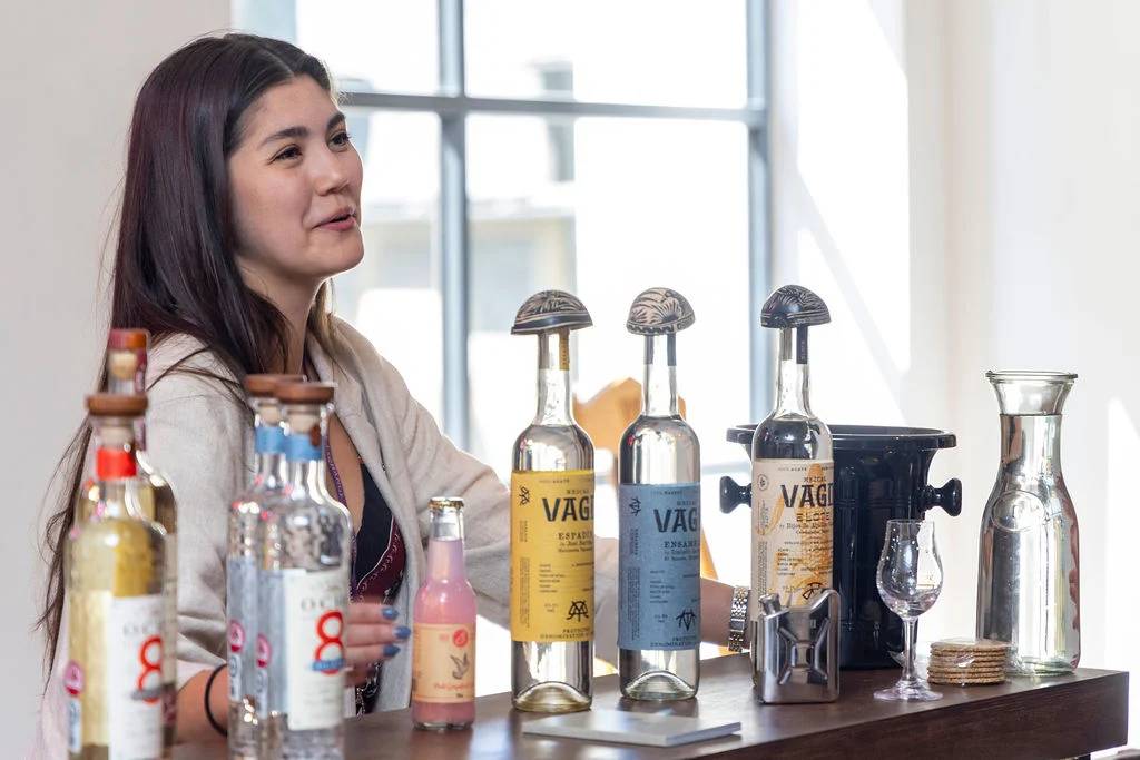 someone at a stand behind a display of tequilas and mezcals