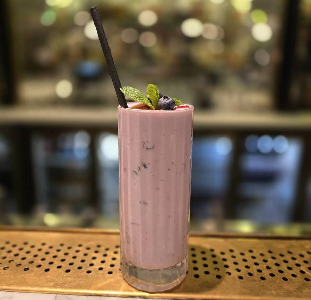 un batido de color rosa coronado con bayas y una ramita de menta