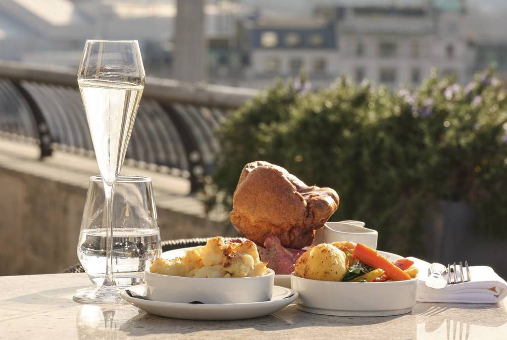 un suculento asado dominical, coronado con un pudín de Yorkshire, acompañado de una copa de champán y con unas impresionantes vistas de Londres desde la azotea de fondo