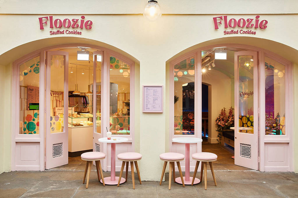 mesas y taburetes rosas fuera de la bonita cafetería Floozie Cookies, con decoraciones y una combinación de colores en amarillo y rosa