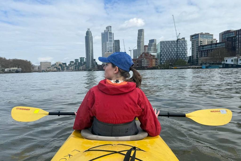 Der Rücken einer Frau in einem Kajak, die auf die Skyline der Stadt auf der Themse blickt