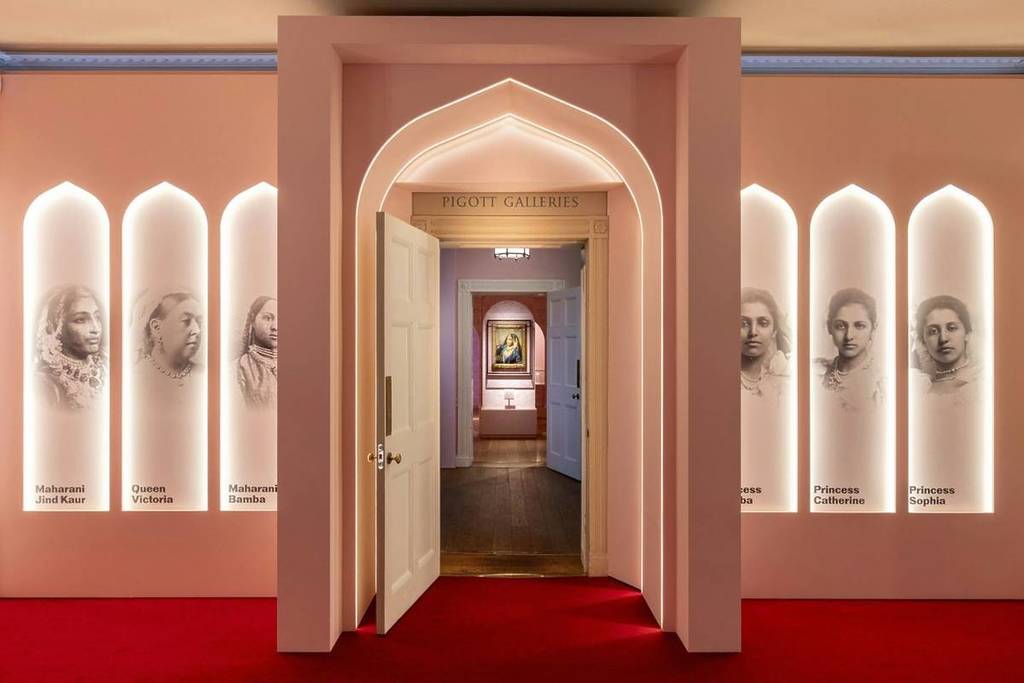 Ein Galerieeingang mit drei Bögen rund um die Tür, auf denen schwarz-weiße Bilder von sechs Frauen zu sehen sind