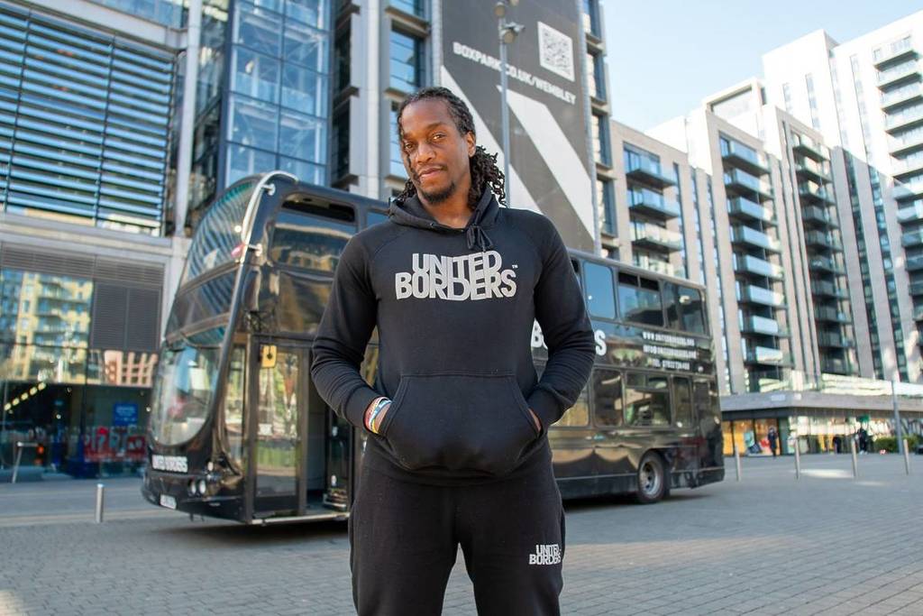 Ein Mann steht in einem Kapuzenpullover vor einem schwarzen Doppeldeckerbus und liest 