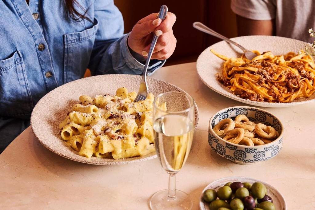 alguien comiendo de un plato de pasta, con otras raciones de pasta y guarniciones dispuestas alrededor del plato sobre la mesa