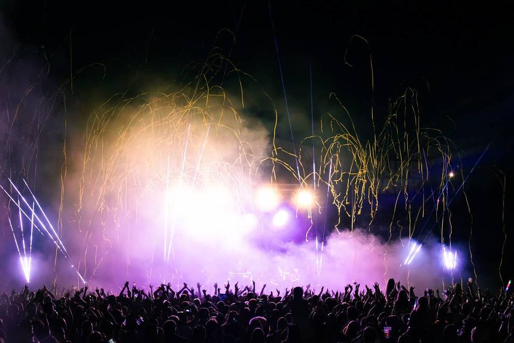 luces brillantes y lluvia de confeti sobre una gran multitud frente al escenario del festival por la noche