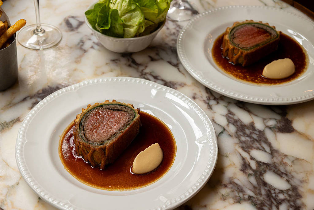 una mesa de mármol con dos bandejas de lonchas de beef wellington perfectamente cocinadas
