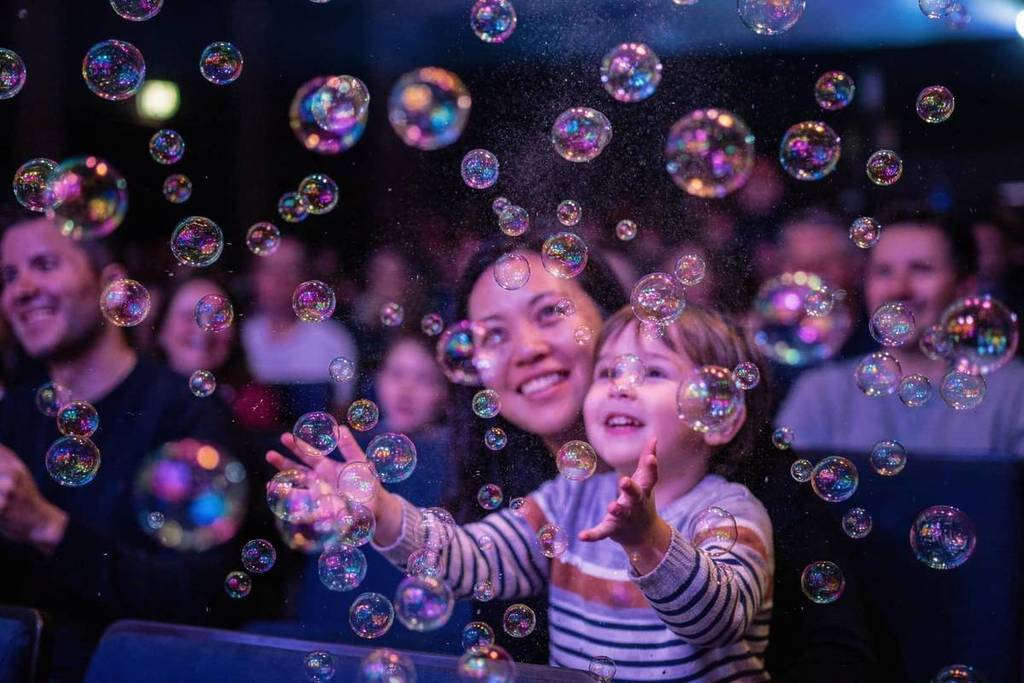 Kind sitzt mit seiner Mutter und spielt mit Blasen auf der BubbleArt Show