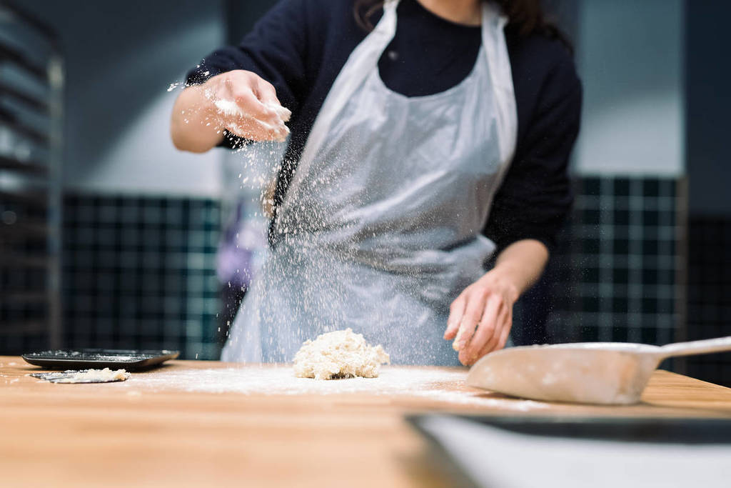 Ein Bäcker streut Mehl auf den Teig auf einem Brett