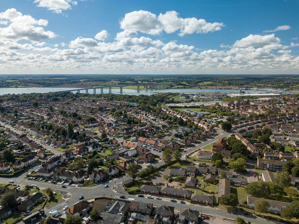 Vista aérea panorámica vertical de casas suburbanas en Ipswich, Reino Unido. El puente de Orwell y el río al fondo. Bonito horizonte nublado.