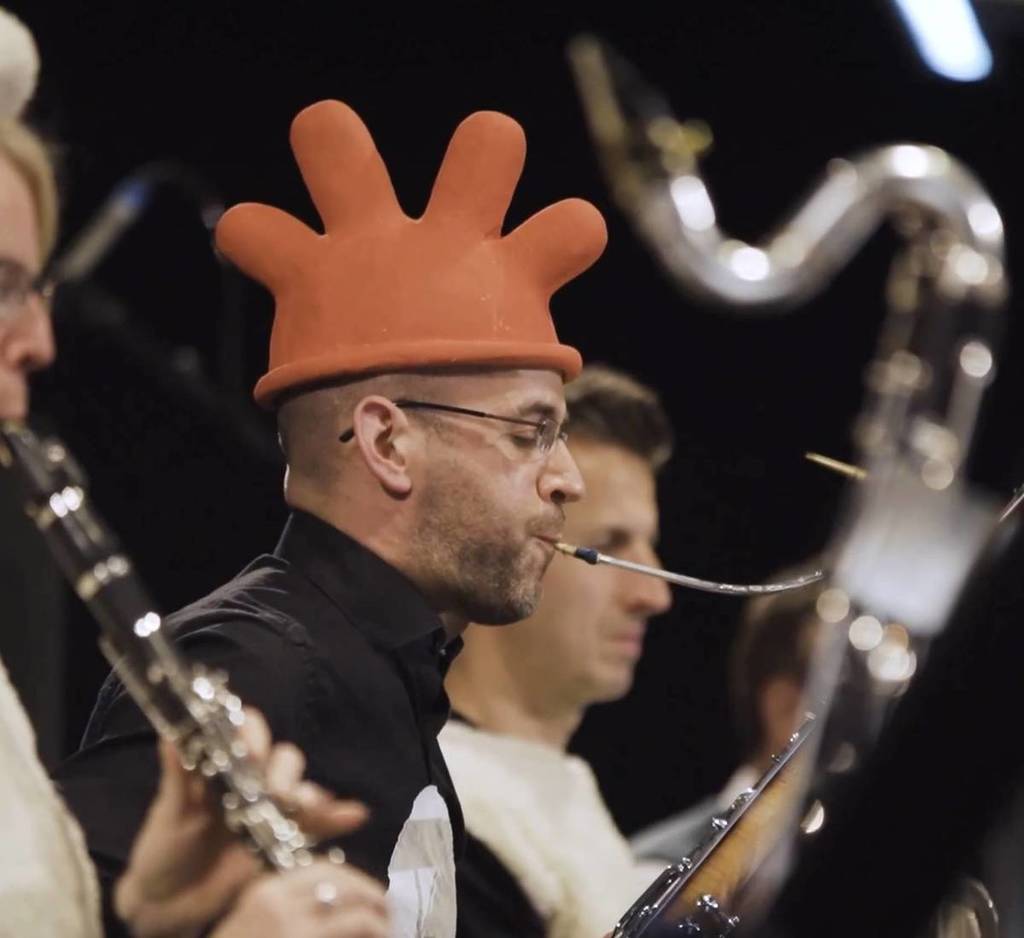 ein Blechbläser, der in einem Orchester spielt und dabei einen handschuhartigen Hut trägt, ähnlich wie Feathers McGraw