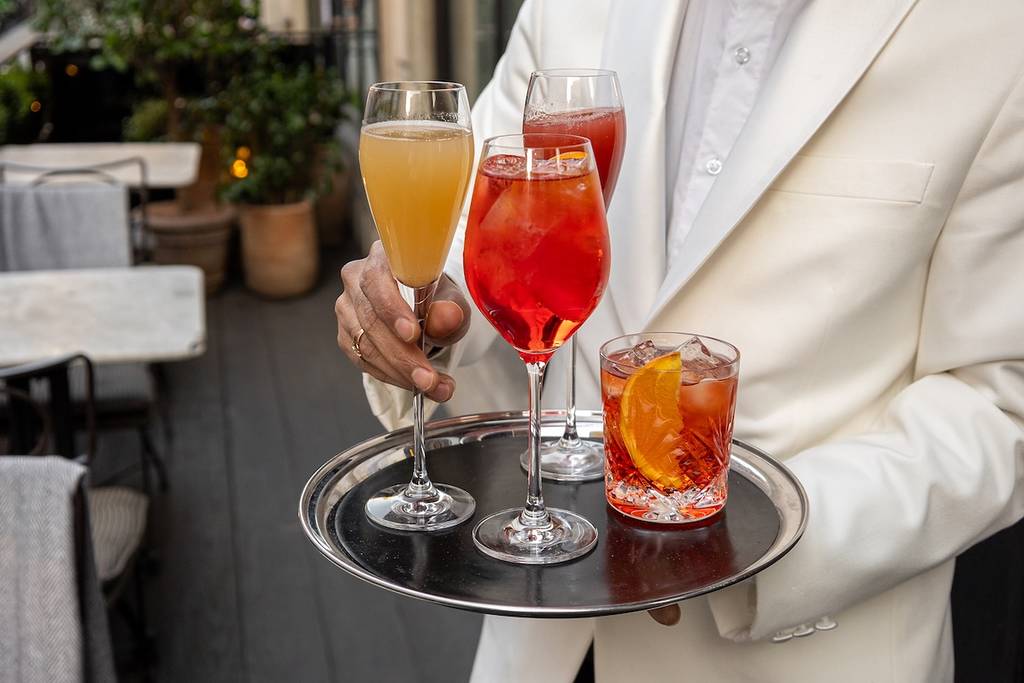 a waitor in a white jacket holds drinks on a silver tray