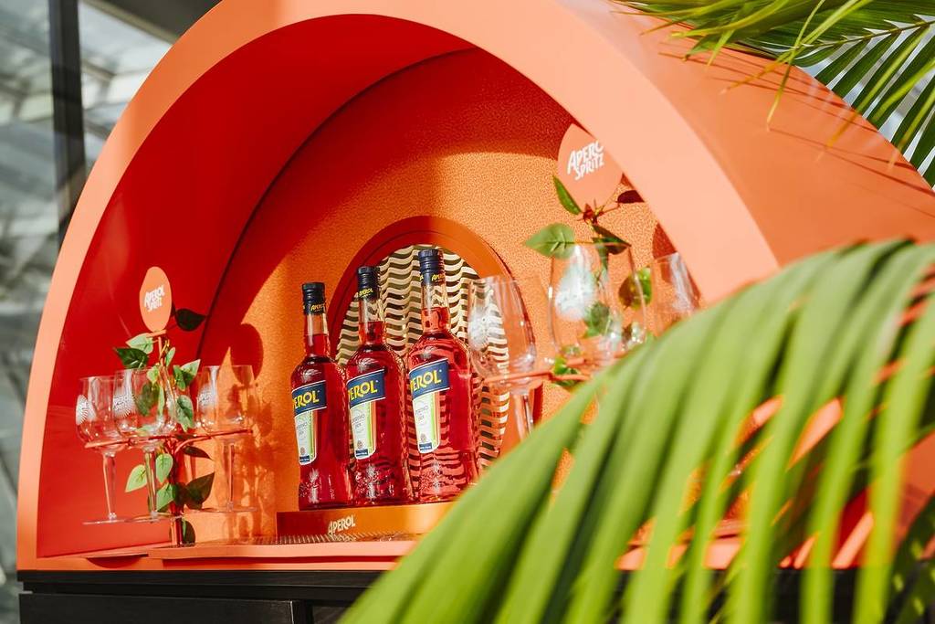an orange shelf with aperol bottles lined up on it