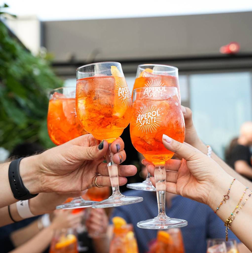 a group of hands meet in a cheers of aperol spritzes