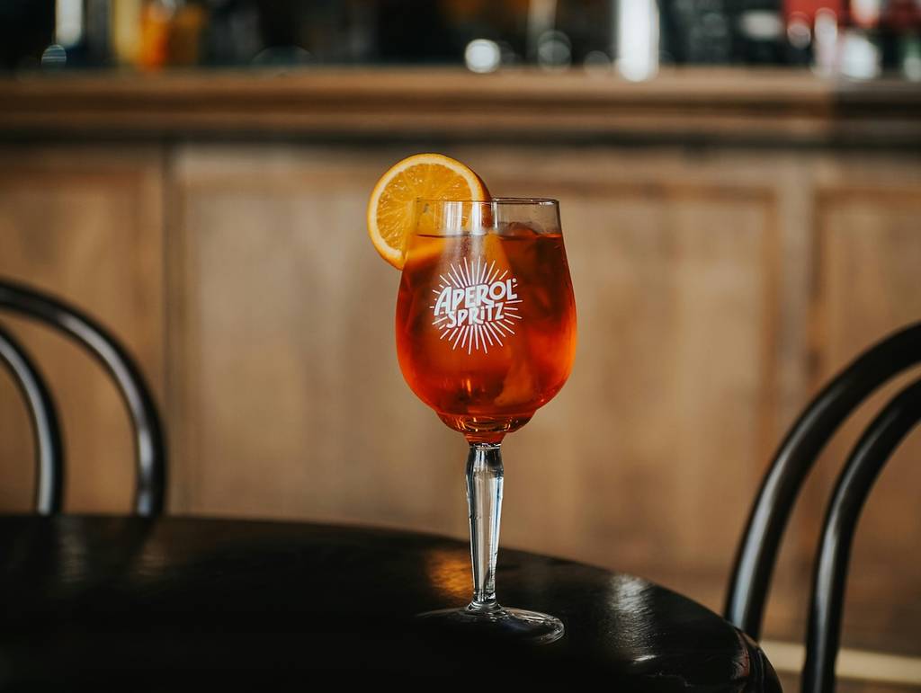 an aperol spritz garnished with an orange slice on a black table at a bar