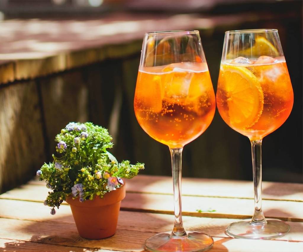 aperol spritz on a wooden table with a small potted plant beside it