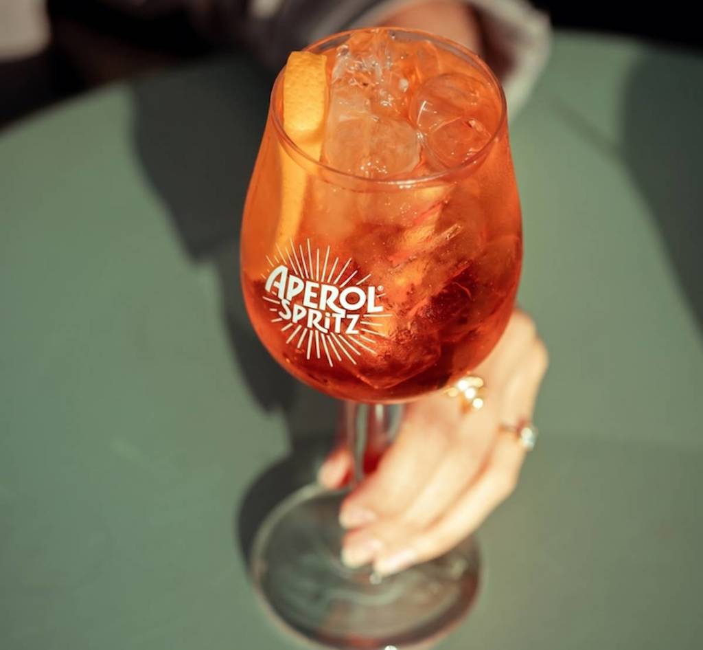 a hand holding an aperol cocktail on a green garden table