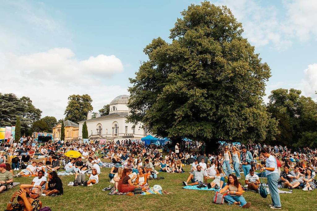 Eine Aufnahme von Menschen, die sich auf Liegestühlen und Picknickdecken an einem Hang im Chiswick House & Gardens entspannen