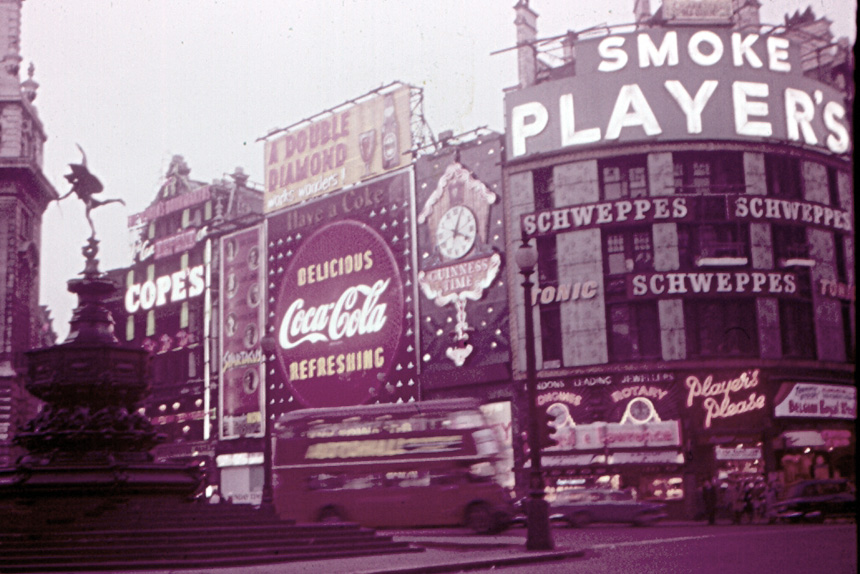 an old photo of piccadilly circus, with vintage ads for coca cola, schweppes, and more adorning the walls