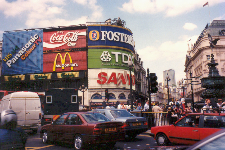 an old photo of the ads covering buildings at piccadilly circus, with cars driving by