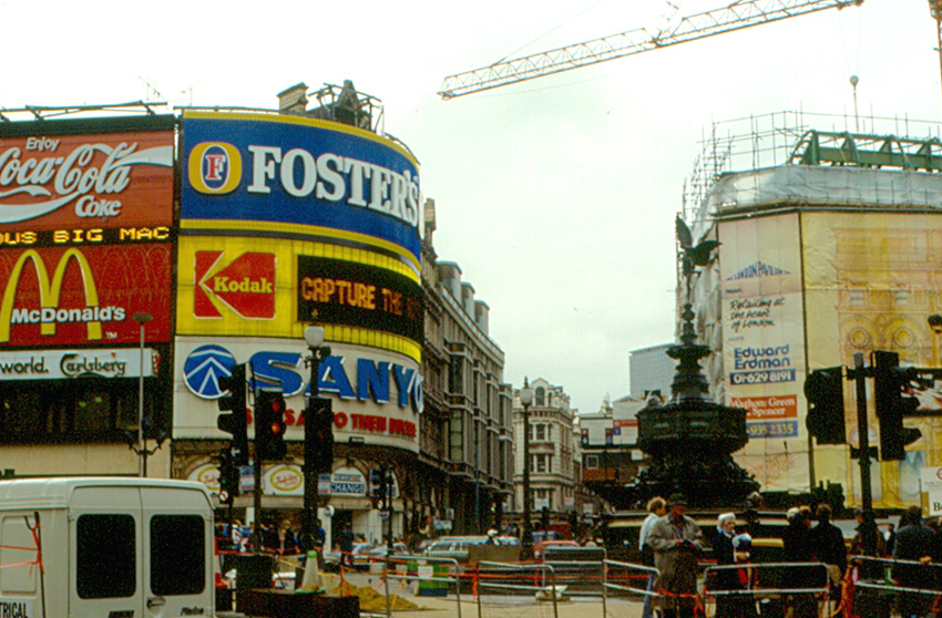 an old photo of the ads covering buildings at piccadilly circus, with cars driving by