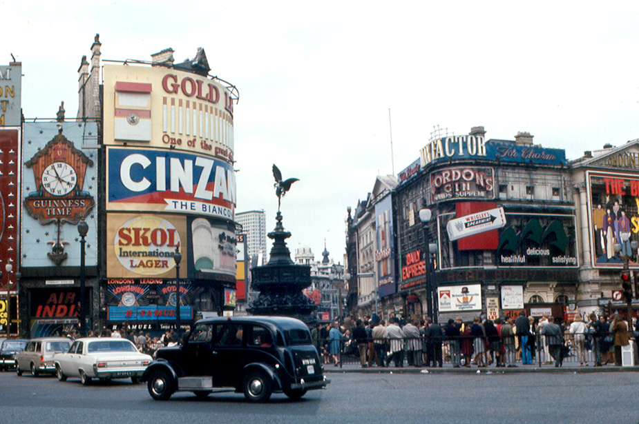 an old photo of the ads covering buildings at piccadilly circus, with cars driving by