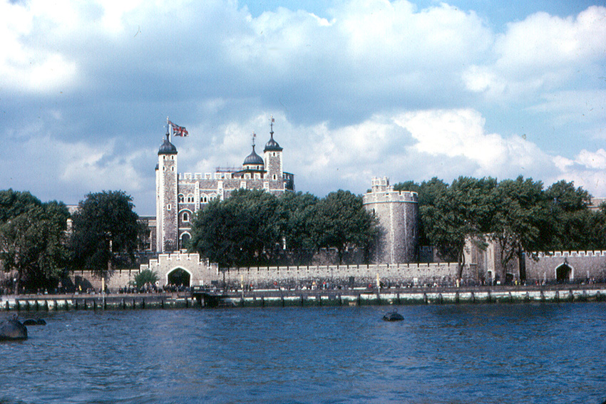 an old photo of the tower of london, seen peeking out from behind trees on the thames bank