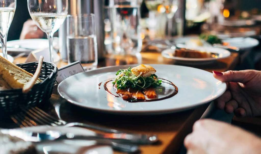 un plateau de nourriture sur une table devant un client, la table comporte de nombreux autres verres et couverts à peine visibles dans les environs
