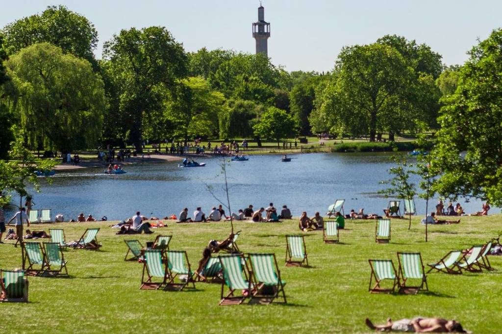 Ein grüner Regents-Park mit verstreuten Liegestühlen, einem See im Hintergrund und Menschen, die sich sonnen