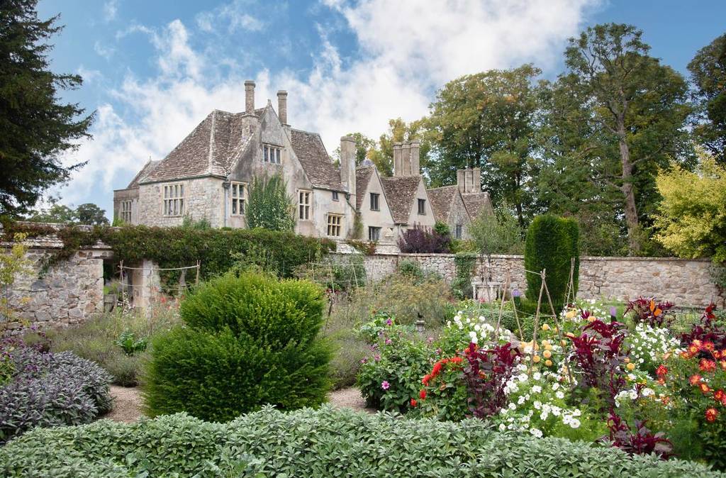 a historic manor house with flowers in the garden in front