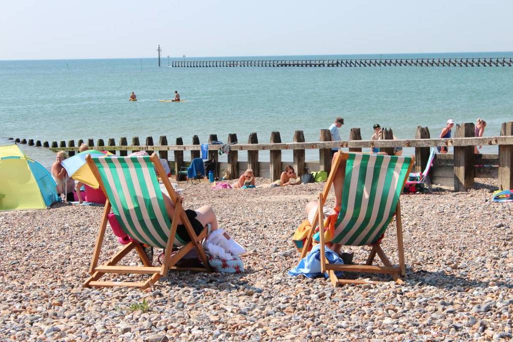 gente sentada en sillas de colores y gente tumbada y paseando por la playa de guijarros de Littlehampton East Beach