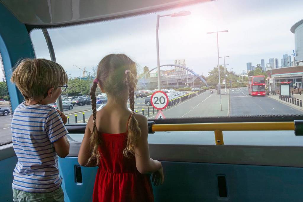 Zwei kleine Fahrgäste blicken aus dem Busfenster auf den Londoner Stadtverkehr und ein sichtbares Tempolimit-Schild und genießen dabei die Aussicht