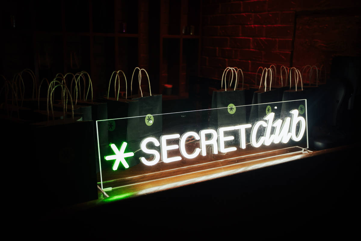 Neon sign with Secret Club logo and name. Set up on a table with goodie bags.